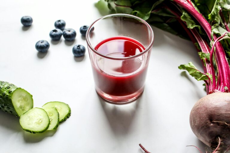 A fresh glass of beetroot juice surrounded by blueberries and cucumber slices.