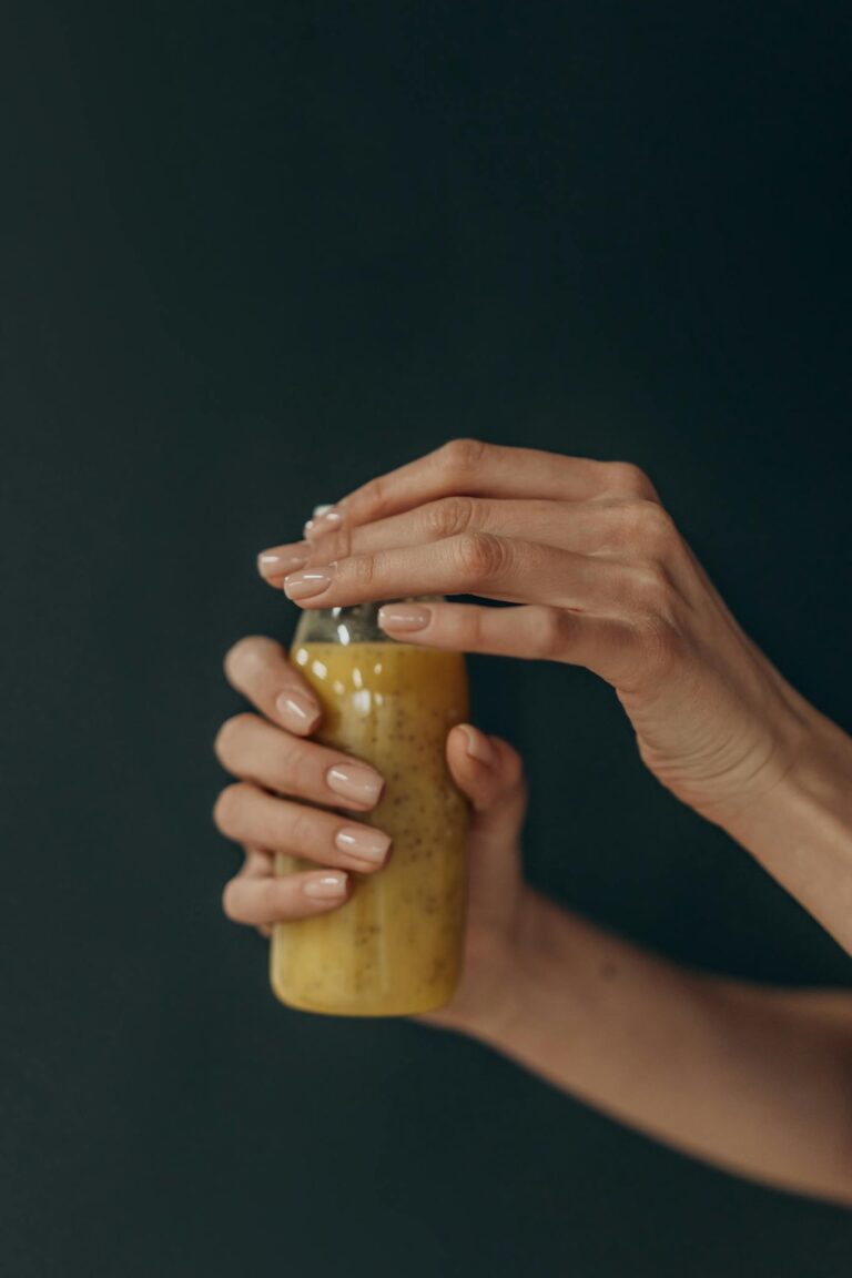 Close-up of a woman's hands holding a refreshing smoothie bottle against a dark background.