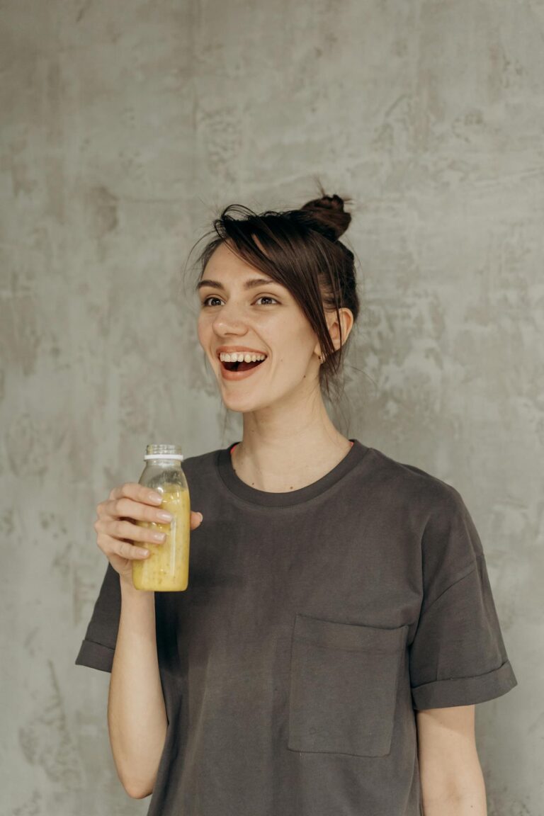 Young woman smiling while holding a refreshing bottle of orange juice indoors.
